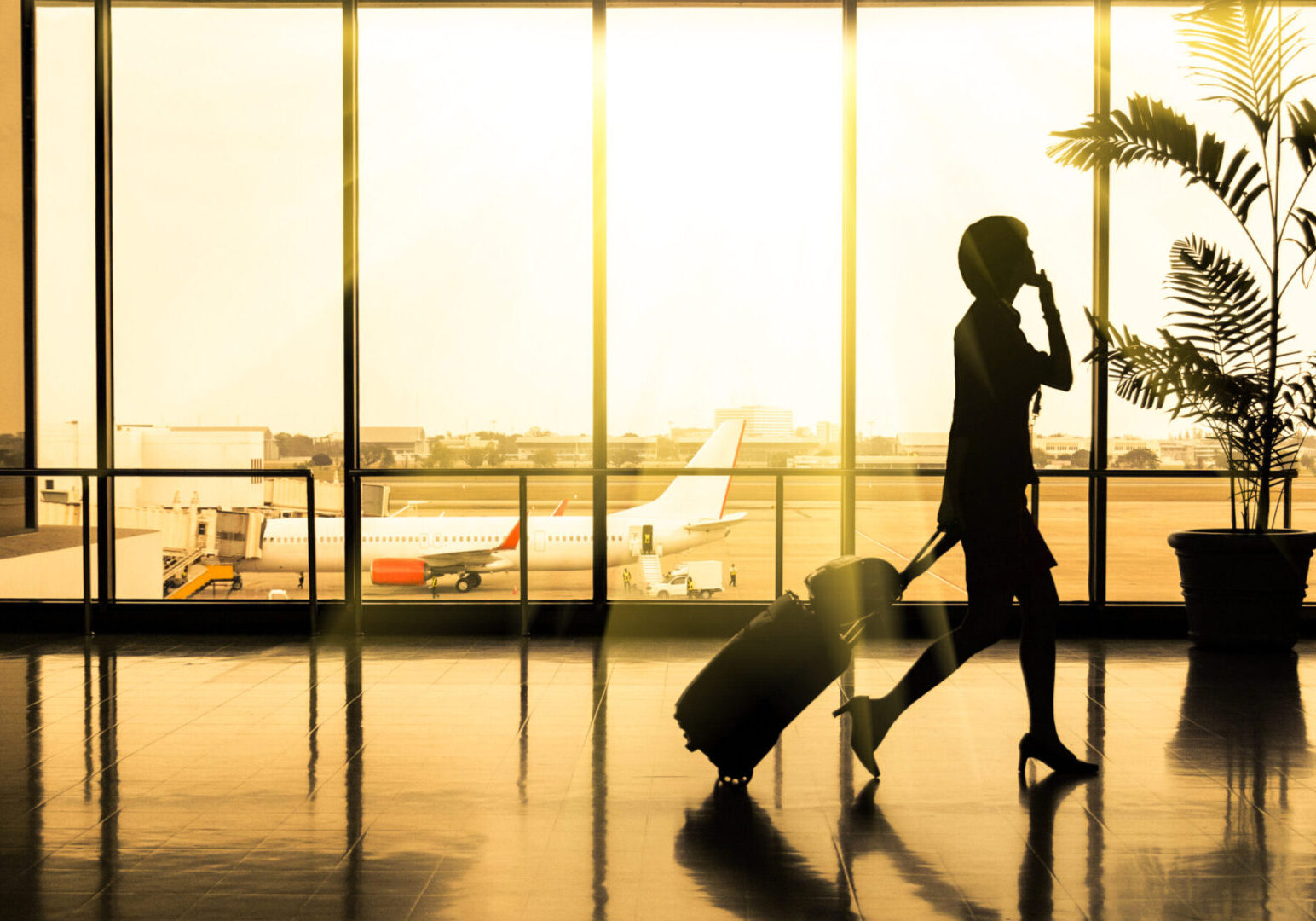 A woman walking through an airport with luggage.